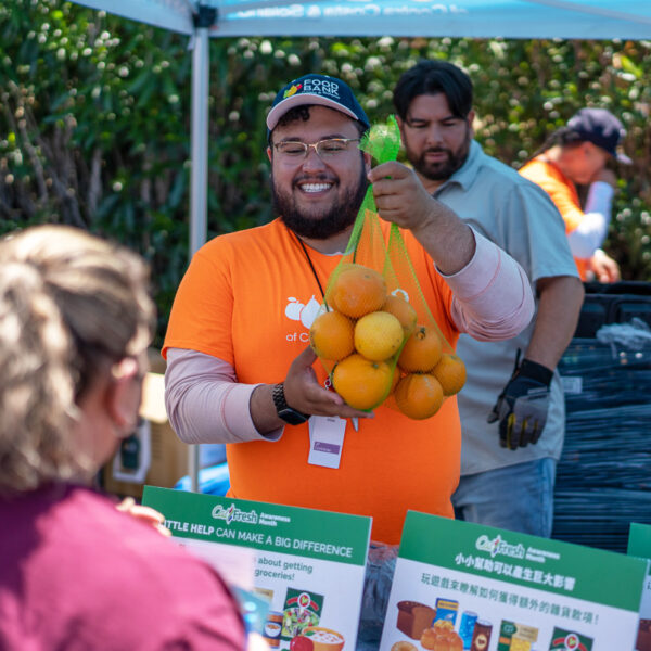 A CalFresh team member in hands a bag of oranges to a woman.