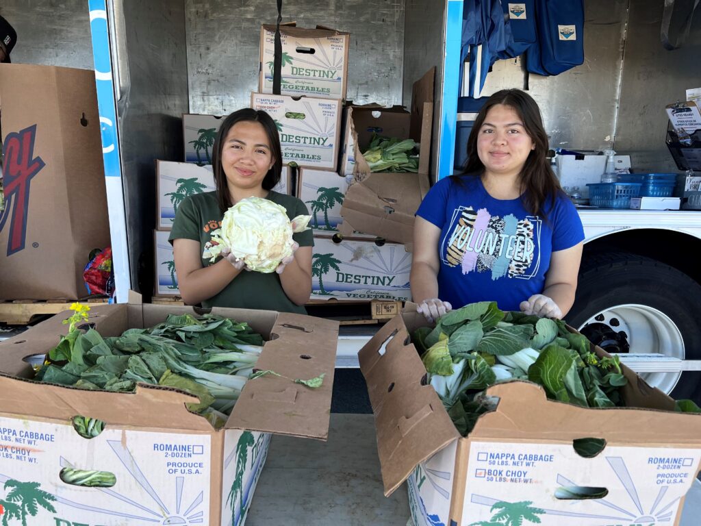 Two young women hand out produce at a Food Bank distribution.