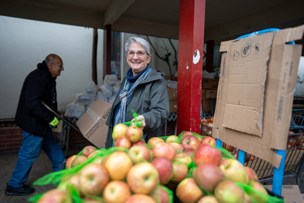 A woman stands behind a pile of apples at Richmond Emergency Food Pantry